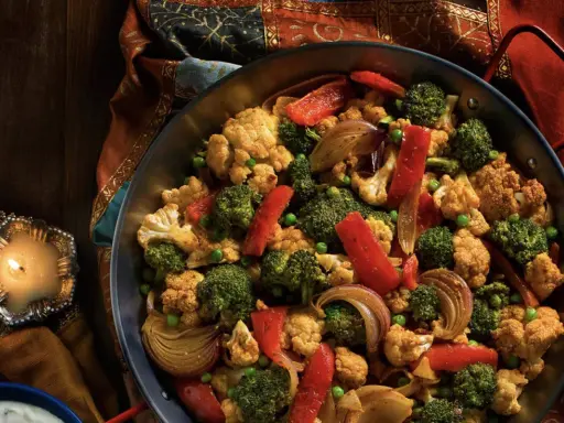 Délicieuse recette choux fleur et brocolis à la poêle, aux poivrons rouges et oignons caramélisés, servie dans un plat, avec une bougie allumée.