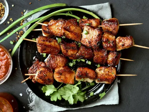 Brochettes de porc mariné, grillées à la perfection, garnies d'oignons verts et de coriandre fraîche. Accompagnées d'une sauce épicée.