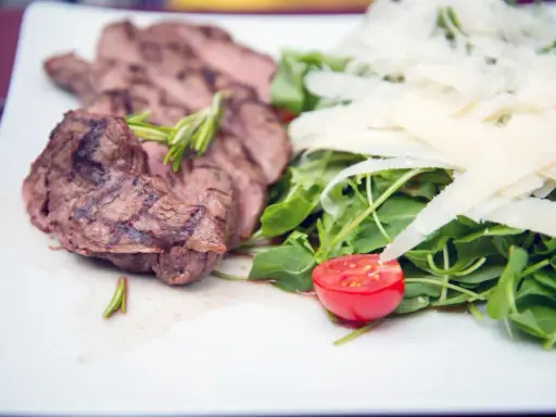 Délicieuse tagliata de boeuf grillée, servie avec une salade verte, copeaux de parmesan et une moitié de tomate cerise.
