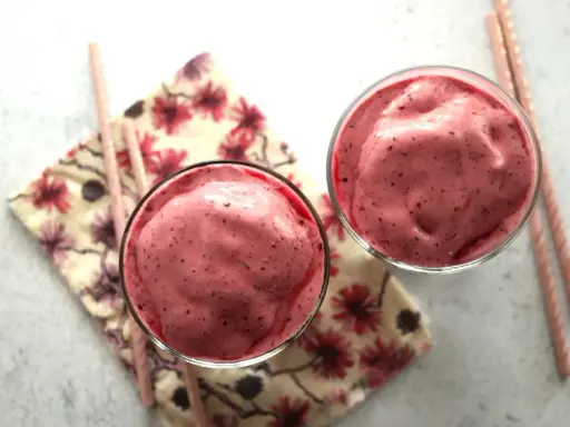 Deux verres remplis d'un onctueux milkshake fruit rouge, accompagnés de pailles roses et d'une serviette fleurie.