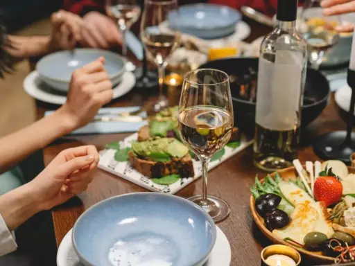 Un verre de vin blanc beurré, des toasts à l'avocat et un plateau de fromages et fruits sur une table dressée pour un dîner convivial.