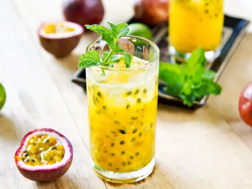 Un verre de cocktail fruit de la passion, garni de menthe fraîche, entouré de fruits entiers et coupés.