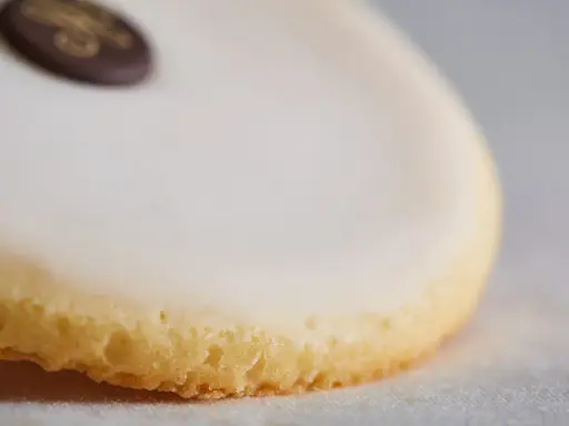 Un palet de dame, biscuit sablé glacé de blanc, orné d'un médaillon chocolat doré.