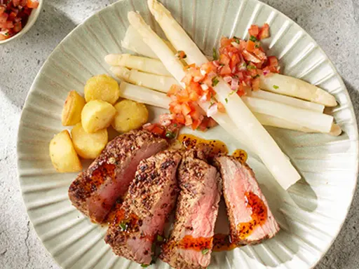 Tranches de viande juteuse avec asperges blanches et pommes de terre sautées, un accompagnement parfait pour un repas savoureux.