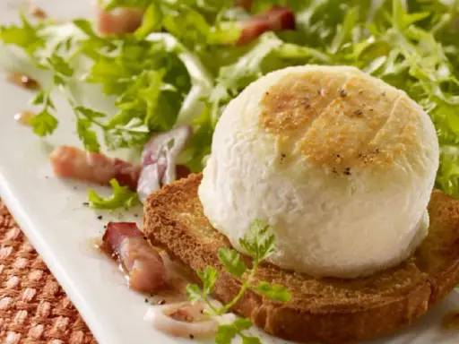 Une délicieuse salade de chèvre chaud sur toast, garnie de lardons et de persil frais, sur une assiette blanche.