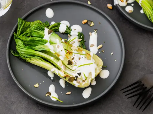 Une assiette de pak choi cru arrosé d'une sauce crémeuse, garni de graines et de zeste de citron vert.