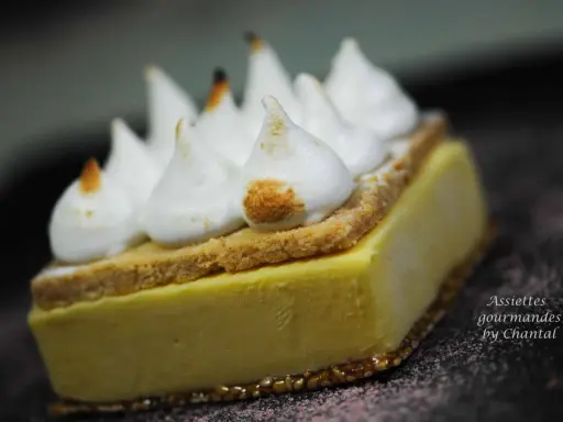 Une tranche de tarte au citron meringuée, avec sa crème jaune pâle, sa fine couche de biscuit et ses pointes de meringue légèrement caramélisées.