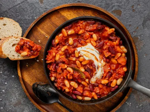 Délicieuse recette baked beans dans une poêle, garnie de crème, servie avec du pain grillé. Un plat réconfortant et savoureux.