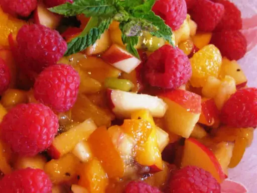 Une délicieuse salade de fruits d'été, pleine de framboises, pêches et abricots juteux, garnie de menthe fraîche.