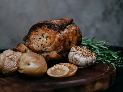 Un délicieux roti de veau au four, accompagné de pommes de terre rôties, d'ail confit, de rondelles de citron et de romarin frais sur une planche en bois.