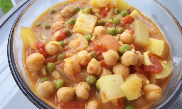Un savoureux curry de petit pois avec des pois chiches et des morceaux de pommes de terre dans une sauce orangée.