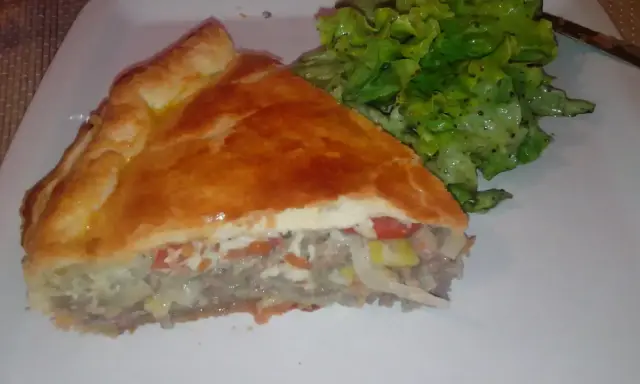 Une part de tourte à la viande grand-mère, dorée et généreuse, servie avec une salade verte croquante. Un délice réconfortant.