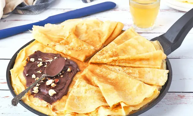 Délicieux crepe a la biere, pliés dans une poêle, garnis de pâte à tartiner au chocolat et noisettes. Une cuillère repose sur le dessus.