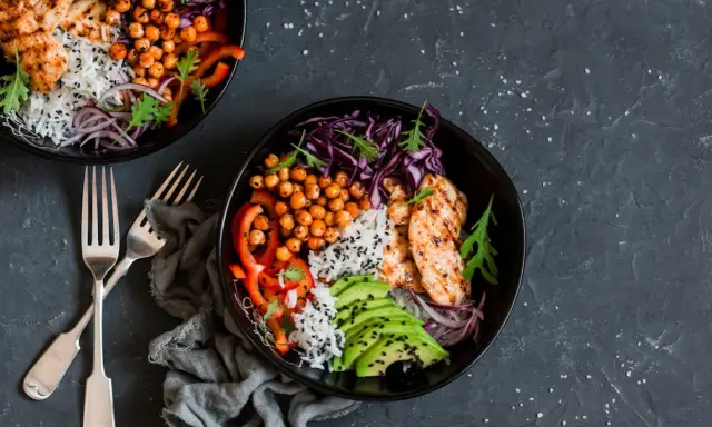 Deux bols de poulet grillé, riz, avocat, pois chiches et chou rouge. Une recette avec salade verte pour un repas sain et coloré.