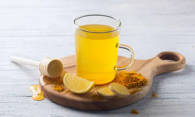 Une tasse de boisson gingembre citron curcuma, avec des tranches de citron, du gingembre frais et du curcuma en poudre.