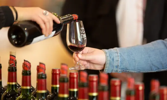 Service d'un vin rouge fruité et doux dans un verre, avec des bouteilles alignées en arrière-plan.