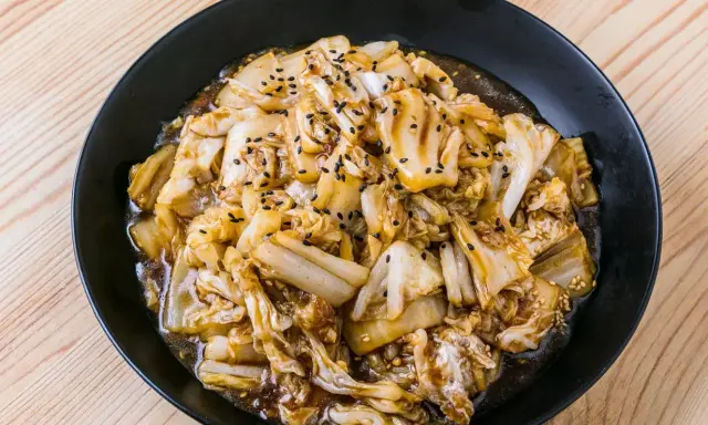 Un plat de recette pak choï sauté, garni de graines de sésame noires et blanches, sur une assiette noire.