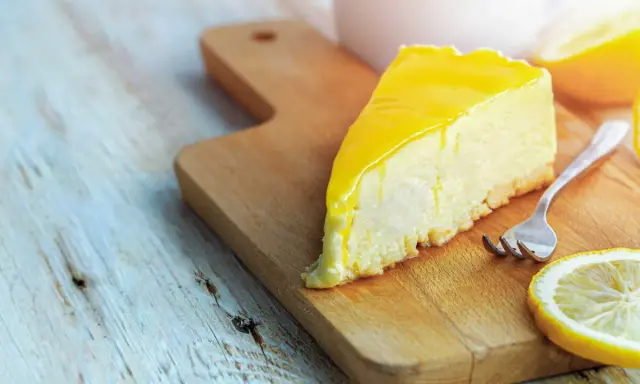 Tranche de cheesecake au citron, une recette Philadelphia sans cuisson, sur une planche en bois avec une fourchette et des rondelles de citron.