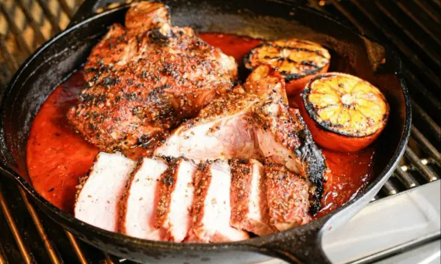 Un savoureux t bone de veau, coupé en tranches, mijote dans une sauce rouge avec des quartiers d'orange grillés dans une poêle en fonte sur un grill.