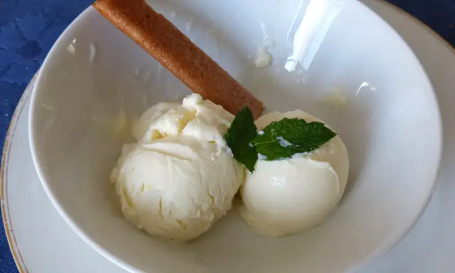 Deux boules de glace au citron onctueuse, garnies de menthe fraîche et d'un biscuit fin, dans un bol blanc.