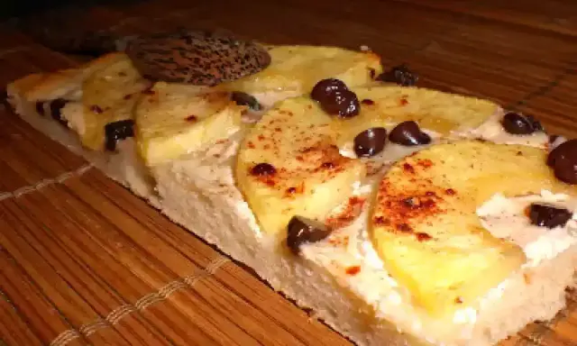 Tranche de tarte flambée sucrée aux pommes, cannelle et pépites de chocolat, posée sur un tapis de bambou.