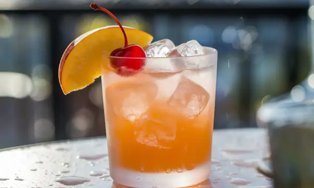 Cocktail rafraîchissant au jus d'abricot et alcool, garni d'une cerise et d'une tranche de pêche.