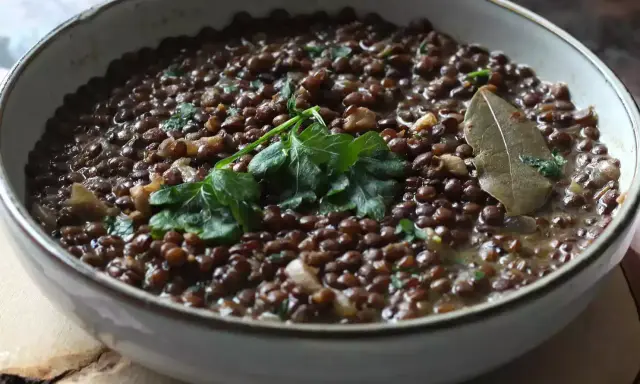 Un plat de cuisson lentilles vertes, garni de persil frais et d'une feuille de laurier.