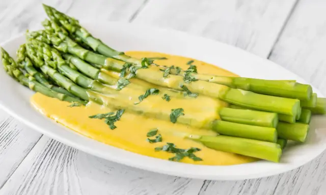 Un bouquet d'asperges vertes nappées d'une sauce hollandaise crémeuse, garnies de persil frais. Une délicieuse idée d'asperges en entrée froide.