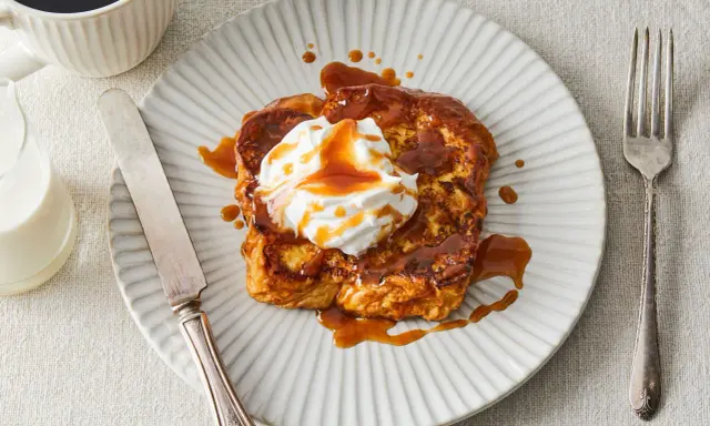 Pain perdu gourmand nappé d'une sauce caramel au miso, garni de crème fouettée. Servi avec une tasse de café et un verre de lait.