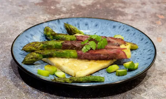 Asperge à la poêle enroulée de viande séchée, servie sur du pain grillé, garnie de persil frais et de morceaux d'asperges.