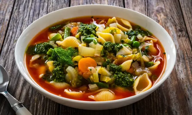Soupe au pistou recette de chef : un plat coloré de légumes frais, pâtes et pesto, servi dans un bol blanc sur fond de bois.