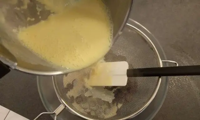 Filtrage de la crème anglaise pour une texture parfaite. Une spatule aide à racler le fond de la casserole.