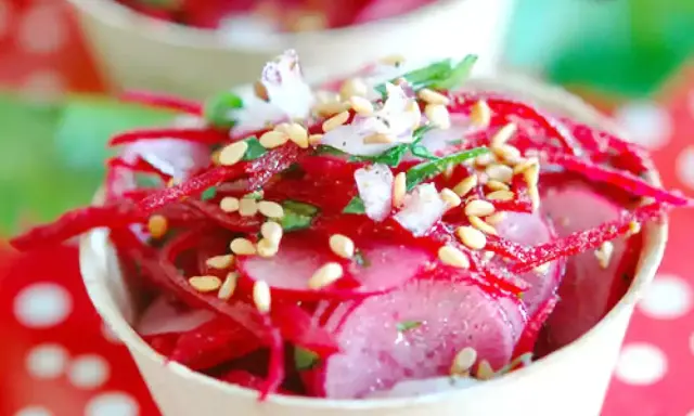 Salade de radis rose râpé et en tranches, garnie de graines de sésame et d'herbes fraîches, servie dans un petit pot.