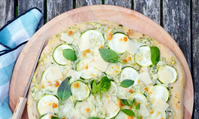 Délicieuse pizza courgette, garnie de fromage fondant, de fines tranches de courgette et de feuilles de basilic frais, prête à être dégustée.