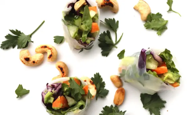 Trois rouleaux de printemps végétariens colorés, remplis de légumes frais et de noix de cajou grillées, parsemés de persil frais.