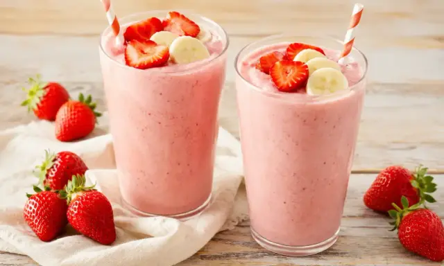 Deux verres de smoothie fraise banane, garnis de fruits frais. Parfait pour une pause gourmande et rafraîchissante.