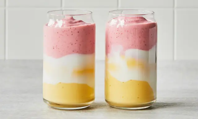 Deux verres de smoothie sans lait aux couches distinctes : jaune, blanc et rose.