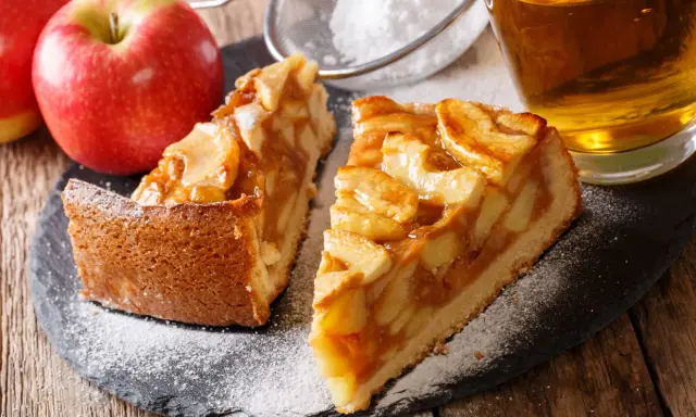 Deux parts de tarte aux pommes, saupoudrées de sucre glace, avec des pommes fraîches et un verre de cidre. Une belle idée de que faire avec des pommes.