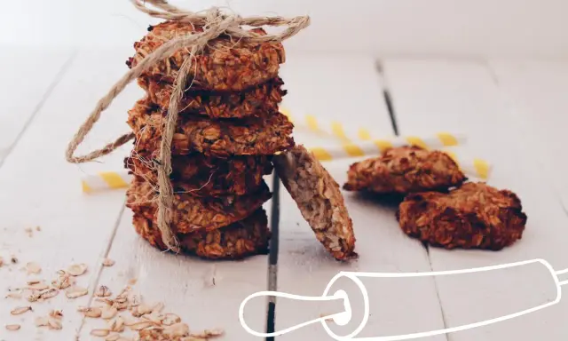 Pile de cookies healthy flocons d'avoine, liés par une cordelette. Quelques flocons éparpillés et des pailles rayées en arrière-plan.