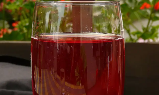 Verre de jus de raisin rouge, pétillant, avec des fleurs rouges en arrière-plan. Parfait pour faire du jus de raisin maison.