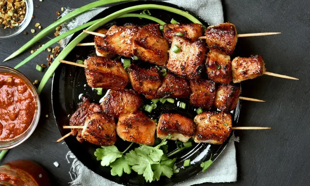 Brochettes de porc mariné, grillées à la perfection, garnies d'oignons verts et de coriandre fraîche. Accompagnées d'une sauce épicée.