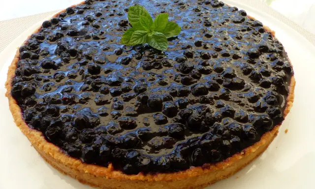 Tarte myrtille amande, une gourmandise aux myrtilles juteuses et à la pâte sablée aux amandes, décorée d'une touche de menthe fraîche.