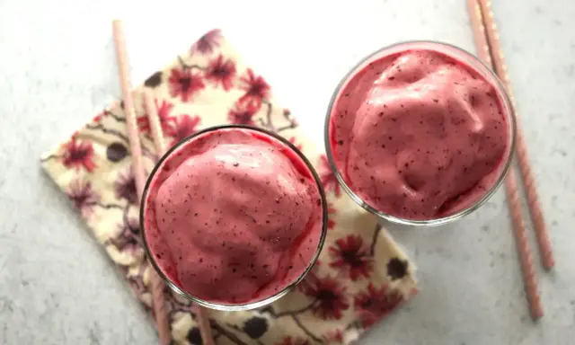 Deux verres remplis d'un onctueux milkshake fruit rouge, accompagnés de pailles roses et d'une serviette fleurie.