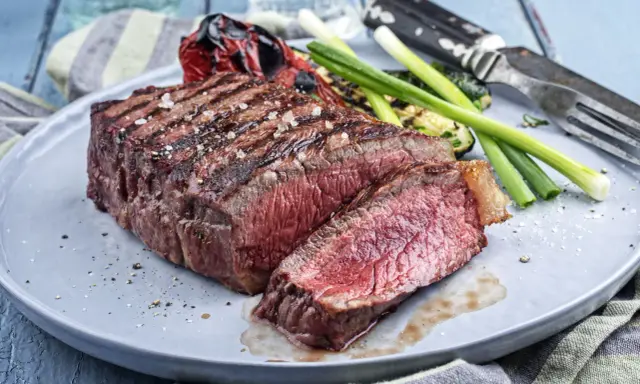 Un savoureux rumsteck de boeuf grillé, coupé en tranches, servi avec des légumes rôtis et des oignons verts sur une assiette grise.