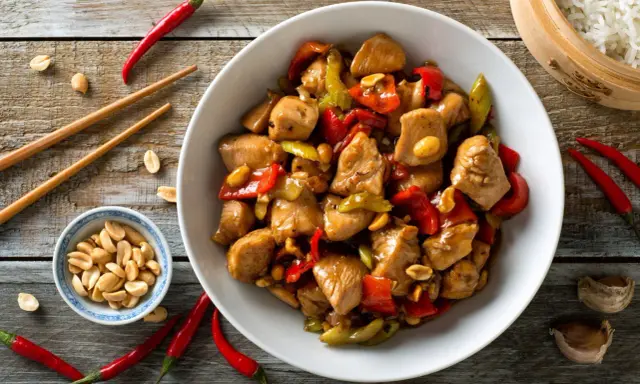 Un délicieux poulet kung pao, garni de cacahuètes croquantes, de poivrons rouges et verts, prêt à être dégusté avec des baguettes.
