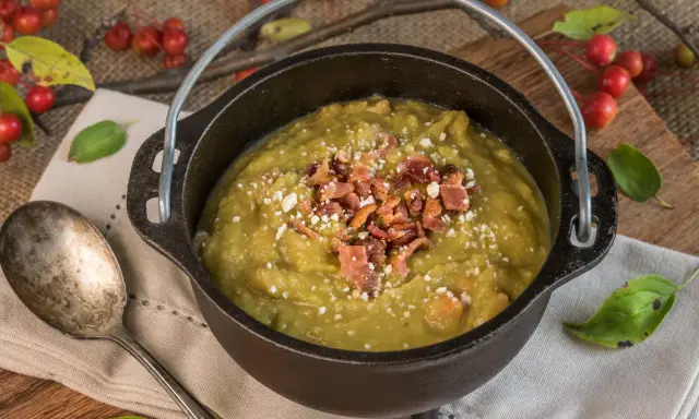 Soupe de pois cassés réconfortante, garnie de lardons croustillants et de fromage râpé, servie dans une cocotte en fonte rustique.