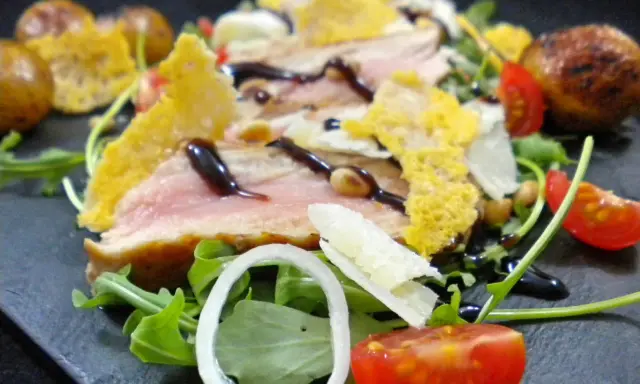 Délicieuse tagliata de veau, servie sur un lit de roquette avec des tomates cerises, des oignons et des tuiles de parmesan croustillantes.