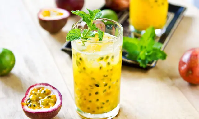 Un verre de cocktail fruit de la passion, garni de menthe fraîche, entouré de fruits entiers et coupés.