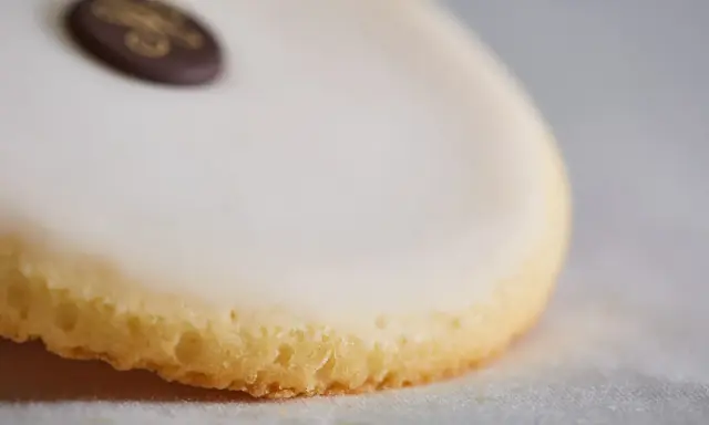 Un palet de dame, biscuit sablé glacé de blanc, orné d'un médaillon chocolat doré.