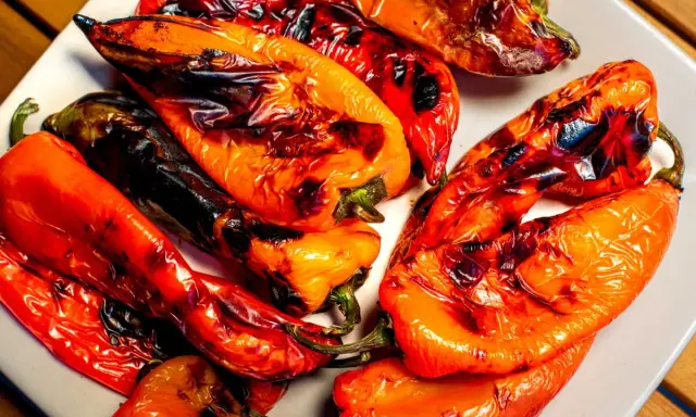 Poivrons rouges et orangés grillés au barbecue, légèrement noircis par la flamme, sur une assiette blanche. Un délice estival.